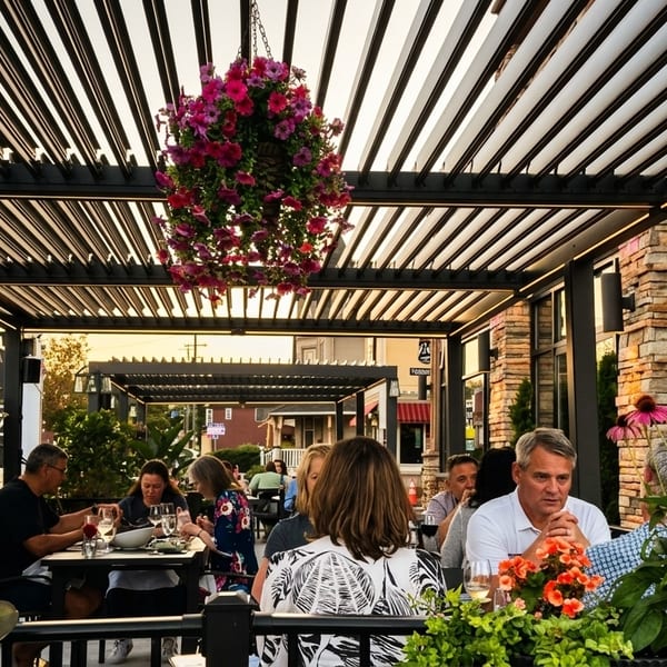 Patrons dine al fresco under a modern pergola adorned with hanging flower baskets at sunset.